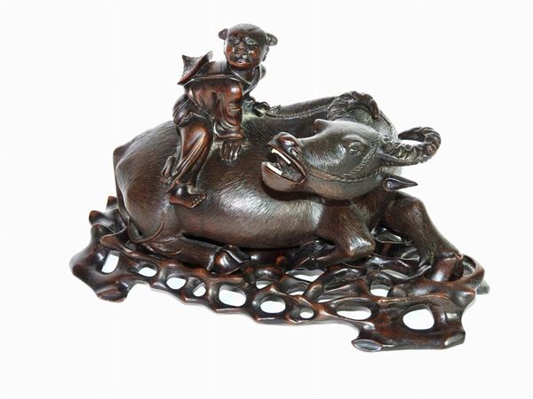A Wooden Sculpture of a Kid Sitting on a Resting Water Buffalo