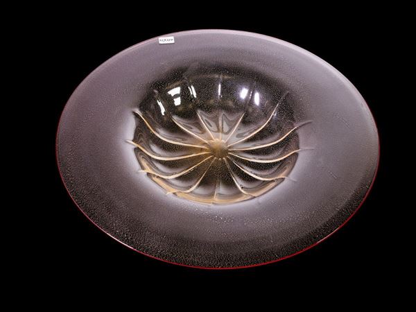 A large blown glass trasparent plate with golden inclusion and red rim applied