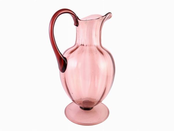 A cyclamen blown glass pitcher with a large handle and stand