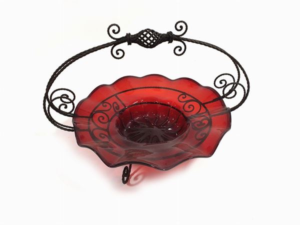 A centerpiece in wavy red blown glass resting on a wrought iron basket.