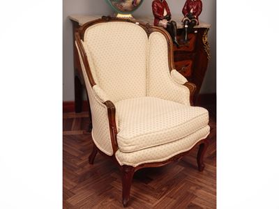 Poltrona bergère in noce, intagli floreali e rivestimento in tessuto color burro